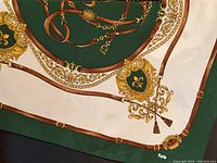 Scarf detail showing hunter green center with brown leather strap print and gold ornamental designs on cream background. Furla logo near edge.