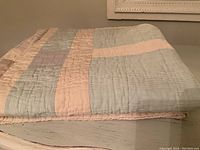 Folded quilt showing pastel stripes and blocks in blue, pink, beige, and lavender colors.