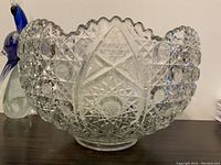 Large cut crystal punch bowl shown on wooden surface, intricate deep cut pattern and scalloped edge visible