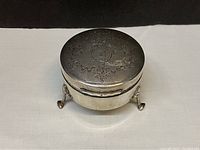 Front and top view of round sterling silver box with engraved lid monogram and floral decoration