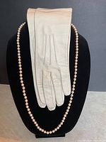 Vintage kid leather gloves paired with costume pearl necklace displayed on black mannequin bust.