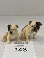 Pair of miniature pug dog figurines sitting side by side on a white fabric surface with lot number card in front.