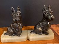 Both bronze Scottish Terrier dog bookends on jade-colored alabaster bases shown side by side on a brown surface with black background.