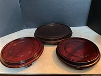 Three rosewood stands arranged on a light surface against a dark backdrop, showing two oval reddish stands and one dark round stand.