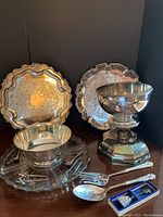 Three silver pieces including scalloped tray, pedestal bowl, and serving platter with utensils.