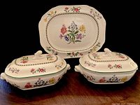 Front view of two large covered serving dishes with floral design and matching serving platter behind them.
