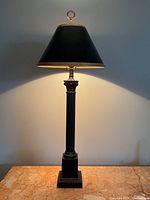 Front view of tall black metal lamp with gold-trimmed shade lit, showing details of column and base.