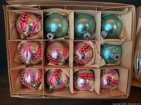 Two packages of vintage Christmas ornaments arranged in divided cardboard boxes. One package contains 12 silver spherical ornaments with pink and red designs, the other has 6 teal spherical ornaments.