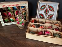 Photo showing vintage bottle brush Christmas tree decorated with colorful glass balls alongside two boxes of vintage glass Christmas ornaments.