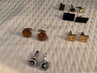 Photo showing all four pairs of vintage cufflinks arranged on fabric background, detailed view of amber, gold-tone, black stone, and silver-tone cufflinks