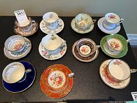 Top view of 10 assorted vintage floral teacups and saucers arranged in two rows on a black surface.