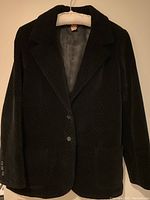 Front view of vintage Anne Klein black velvet jacket hanging on a hanger, showing structured blazer style with lapels and two front buttons.