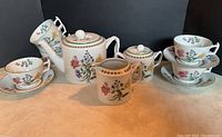 Full tea set showing teapot, cream pitcher, sugar bowl with lid, 3 tea cups with saucers, and 4 extra cups stacked to the left.