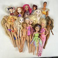 Top view of 17 dolls including Barbie, Ken, fairy-themed dolls, some clothed and some nude, with a variety of hair colors and styles.