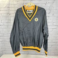 Full front view of the dark grey Boston Bruins vintage NHL jersey with yellow and black V-neck collar, cuffs, and waistband, hanging on a plastic hanger against brick wall background.