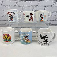 Front view of 6 Disney-themed mugs arranged on two levels, showcasing various Mickey Mouse graphics and themes