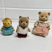 Three small flocked animal figurines on white surface against white brick background.