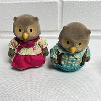 Two small flocked owl figurines, one female and one male, posed side by side on a white textured surface.