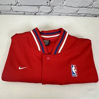Folded red Philadelphia 76ers NBA Nike jersey with NBA and Nike logos on front and striped collar.