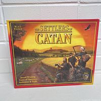 Front cover of Settlers of Catan game box showing artwork of settlers and fields at sunset.