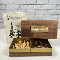 Photo of the wooden Grandmaster chess set original box with the chess pieces inside and instruction booklet behind it.