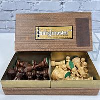 Open wooden box showing dark and light chess pieces inside, label on lid visible