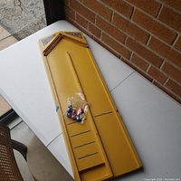 Top-down view of the yellow rebound game board on white folding table, showing scoring sections and bag of metal balls
