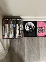 Photo showing 11 Playstation 2 game cases stacked and one game case opened to show disc and manual, revealing condition and titles.