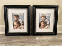 Two black photo frames side by side on floor, each holding placeholder photo with a man and boy. Frames have a beaded black border.