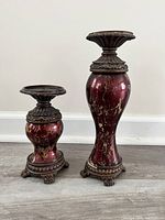 Two red marble candle holders on floor, showing overall size and shape with ornate bronze bases and tops, one taller and one shorter.