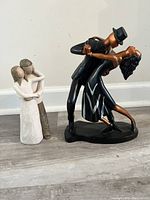 Two hand-painted sculpted figure couples shown together, one dancing with man in black suit and top hat, the other embracing couple in neutral tones.