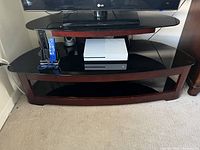 Front view of TV stand holding a television and media devices on the glass shelves.