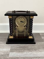 Front view of the antique quartz tabletop clock with black body, twisted columns, and gold accents, clock face visible with Roman numerals.