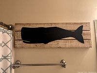 Frontal image of blue metal whale wall art on wood plank background showing size and detail.