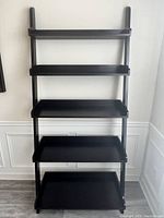 Front view of the black wooden bookstand ladder with all five shelves visible against wall.