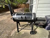 Full view of smoker on patio showing barrel chamber, chimney stack, side firebox, wheels and bottom rack