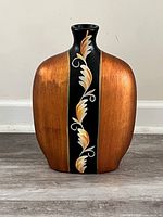 Front view of the wooden vase showing the orange sides and black central vertical strip with floral design.