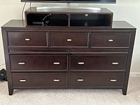 Front view of brown chestnut finish wooden dresser with nine drawers and TV box on top.