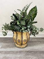 Front angled view of metal vase with artificial greenery arrangement.