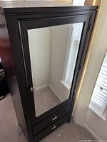 Front-side view of the brown chestnut finish wooden armoire with full-length mirror door and two drawers beneath.