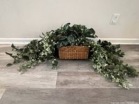 Artificial Pothos plant in rectangular brown basket displayed on floor with trailing foliage extending outward.