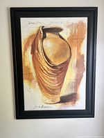 Framed artwork showing orange vase abstract print on a cream background, in a black beaded frame hung on white wall.