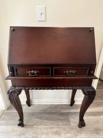 Secretary desk closed showing front panel with ornate wood and hardware, carved legs.