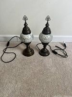 Pair of Turkish metal mosaic globe table lamps with white mosaic glass on bronze metal bases shown unplugged on carpeted floor.