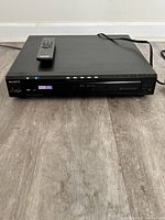 Front view of the black Sony DVD player with remote on top, showing power indicator and display screen.