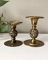 Front view of the mismatched vintage brass candlestick holders showing intricate openwork details on bases and spherical centers.