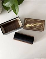 Photo of wooden base with velvet cleaning surface, removable wooden block, and the original branded box with gold text.