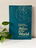 Front cover of the National Geographic Atlas of the World, Seventh Edition, showing blue cover with globe outline and gold text.