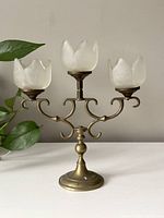 Front full view of the vintage brass candelabra showing three arms with frosted glass tulip shaped candle holders, standing on round base.