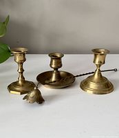 Three brass candlesticks and one candle snuffer arranged on a surface with a neutral background.